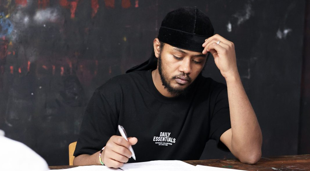 Mohamed sitzt nachdenklich an einem Tisch und macht sich Notizen.