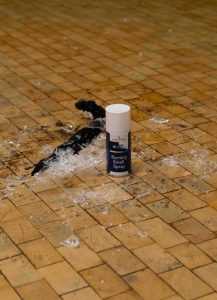 Auf dem Bild sieht man einen kleinen Scherbenhaufen und eine Sprühdose, die daneben steht. Auf der Sprühdose steht Brandgeruch Spray.