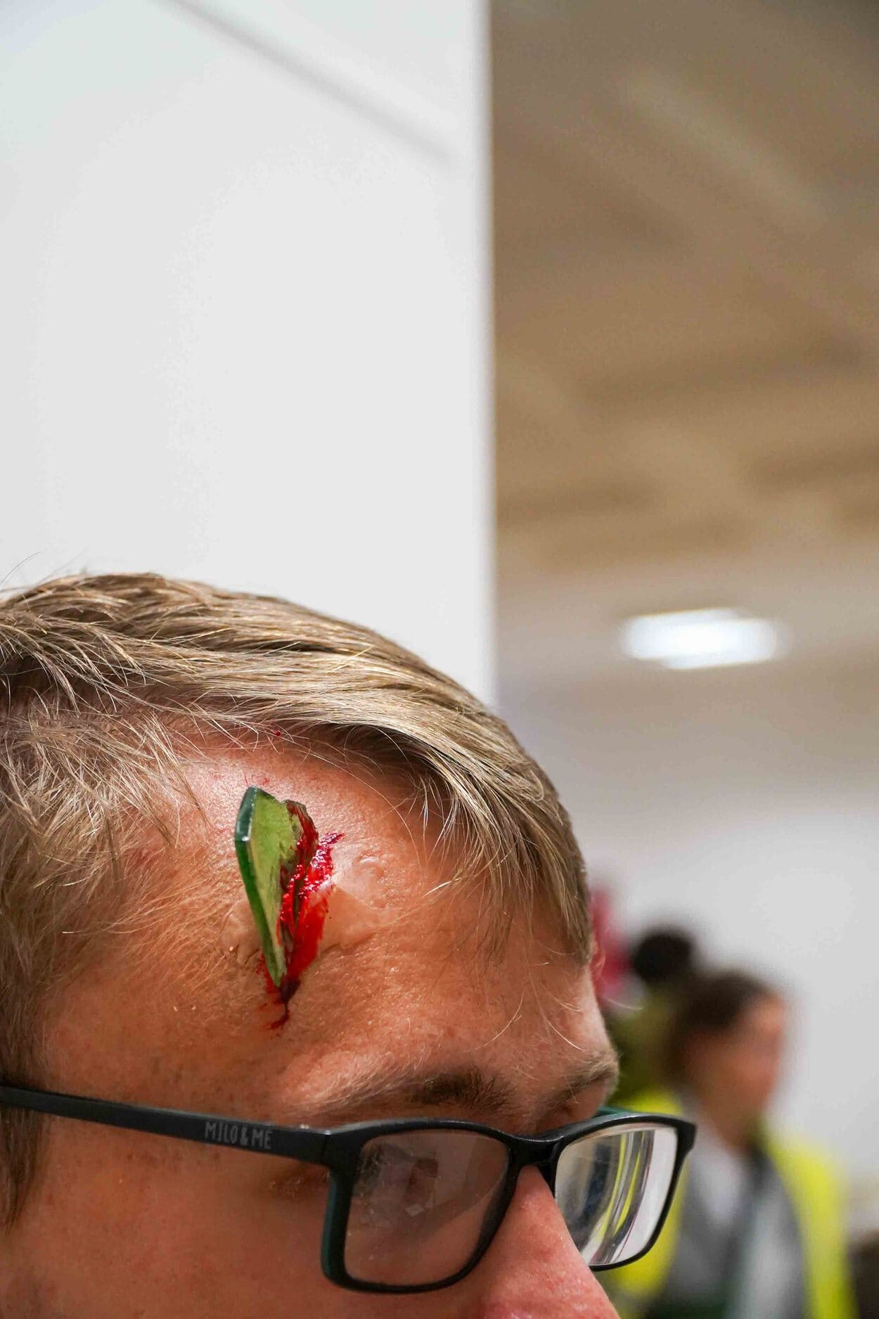 Auf dem Bild sieht man, wie einem Mann mit Brille eine Glasscheibe im Kopf zu stecken scheint. Die Verletzung wurde einem der Darstellenden der Übung geschminkt.