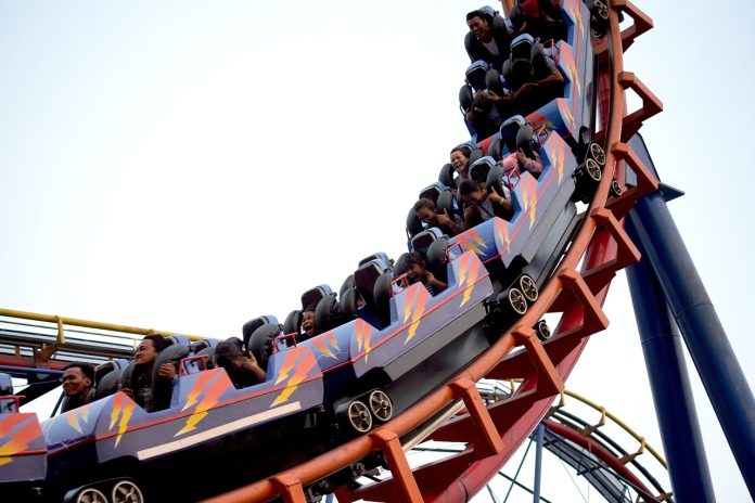Ausschnitt einer fahrenden Achterbahn mit mehreren Personen, die in den Wagen sitzen.