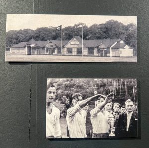 An einer schwarzen Wand hängen untereinander zwei kleine Bilder. Das obere Bild zeigt ein Verinshaus. Das untere Bild zeigt drei junge Fußballspieler, die den Hitlergruß machen.