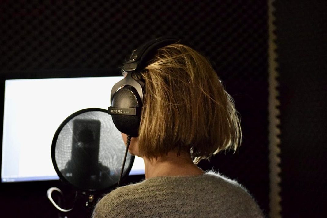 Hinterkopf einer Frau mit Kopfhörern vor ihr steht ein Mikrophon.