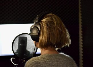 Wer spricht hier eigentlich? Hinterkopf einer Frau mit Kopfhörern vor ihr steht ein Mikrophon.