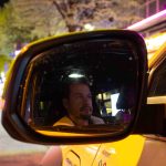 „Beichtvater und Therapeut”: Unterwegs mit einem Taxifahrer Die Spiegelung von dem Taxifahrer Daniel Lebastchi in dem Seitenspiegel seines gelben Taxis. Im Hintergrund ist die Reeperbahn zu erkennen.