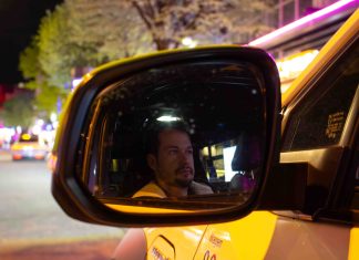 „Beichtvater und Therapeut”: Unterwegs mit einem Taxifahrer Die Spiegelung von dem Taxifahrer Daniel Lebastchi in dem Seitenspiegel seines gelben Taxis. Im Hintergrund ist die Reeperbahn zu erkennen.