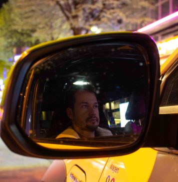 „Beichtvater und Therapeut”: Unterwegs mit einem Taxifahrer Die Spiegelung von dem Taxifahrer Daniel Lebastchi in dem Seitenspiegel seines gelben Taxis. Im Hintergrund ist die Reeperbahn zu erkennen.