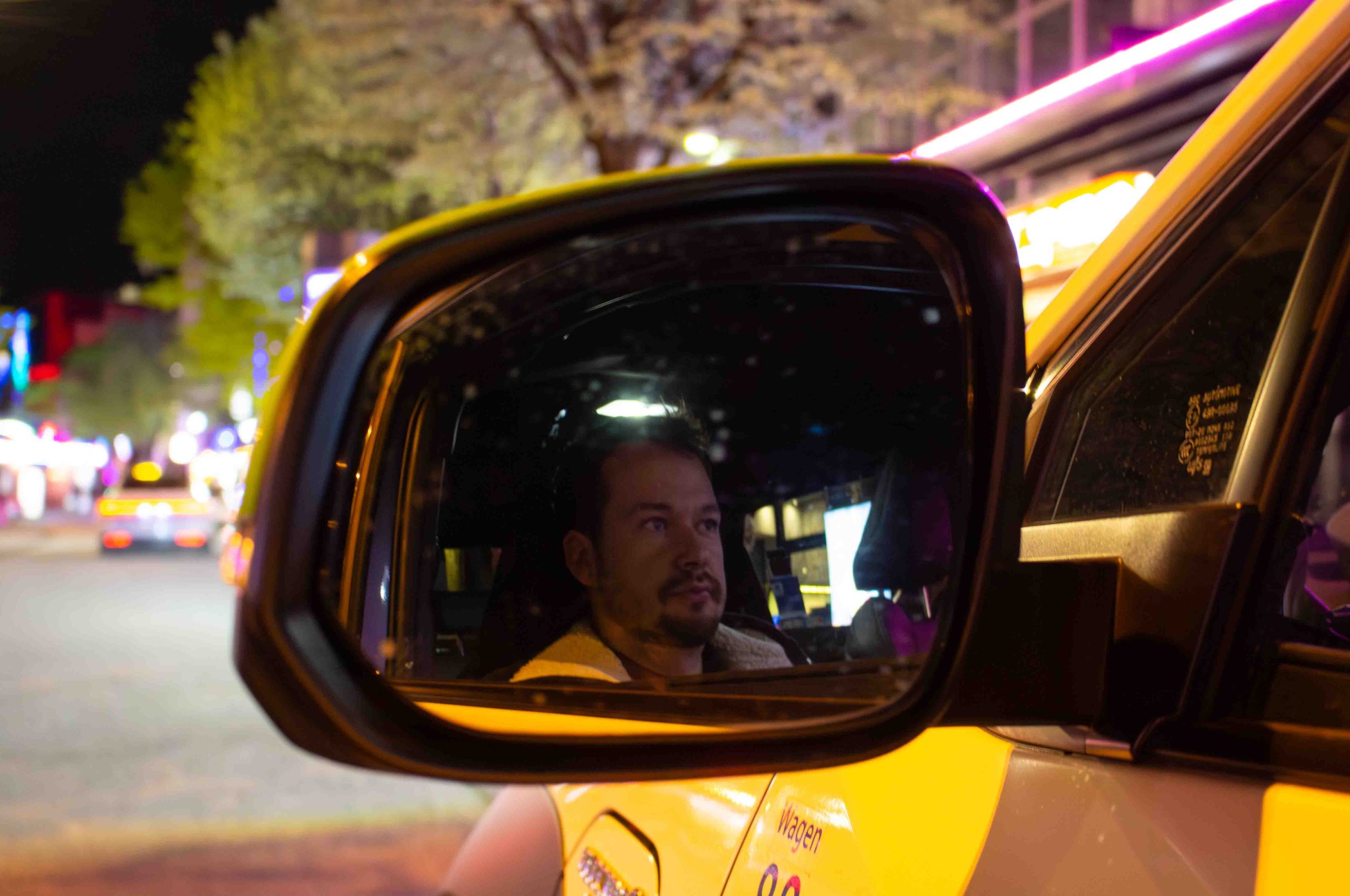 Daniel Lebastchi im Taxi Die Spiegelung von dem Taxifahrer Daniel Lebastchi in dem Seitenspiegel seines gelben Taxis. Im Hintergrund ist die Reeperbahn zu erkennen.