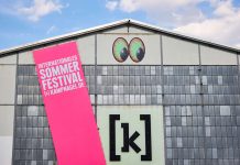 Kampnagel Sommerfestival: Das große Hoffen Die Kulturfabrik Kampnagel in Winterhude mit einem großen pinken Banner, auf dem Sommerfestival in Großbuchstaben steht.