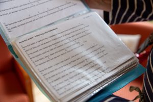 Ein blaues Liederbuch ist aufgeschlagen. Auf den Seiten sind Texte und Noten für eine Ukulele vermerkt.