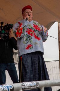 Queeraktivistin Didine van der Platenvlotbrug steht mit Mikrofon in der Hand auf der Bühne der "Come on, Boys!" Demo.