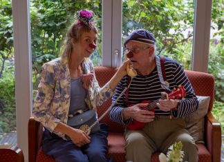 Ein Clown im Pflegeheim: „Mögt ihr Plattdeutsch?“ „Jaaaaa!“ Martin Schneider-Schall und Franziska Heuschkel sind Clowns im Pflegeheim. Sie tragen bunte Klamotten sowie eine rote Plastiknasen und sitzen auf einem Sofa zusammen.