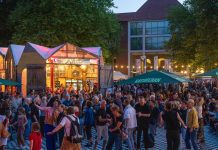 Kostenlos Kultur! Die Altonale startet Das Bild zeigt viele Menschen, die in der Abenddämmerung draußen stehen und tanzen. Im Hintergrund sind bunt beleuchtete Gebäude zu sehen.