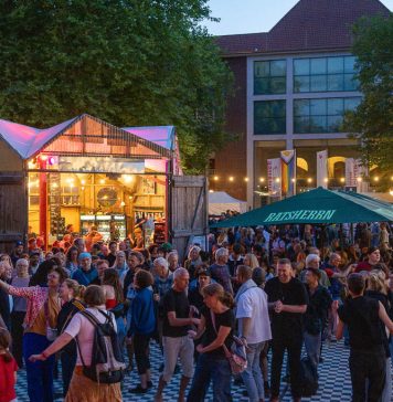 Kostenlos Kultur! Die Altonale startet Das Bild zeigt viele Menschen, die in der Abenddämmerung draußen stehen und tanzen. Im Hintergrund sind bunt beleuchtete Gebäude zu sehen.