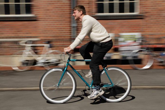 Das Bild zeigt einen Mann der auf einem hellblauem Fahrrad fährt. Er ist scharf zu erkennen, der Hintergrund ist unscharf.