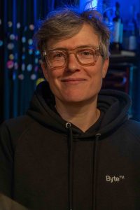 Das Portrait einer grauhaarigen Frau mit Brille und schwarzem Hoodie. 