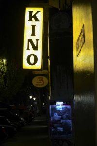 Ein glebes Leuchtschild mit der Aufschrift "Kino" in dunkler Umgebung. 
