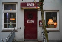 Kino, günstiger als Netflix Eine Neonröhre wirft von oben Licht auf eine rote Tür, in deren Mitte eine Filmrolle hängt und die Aufschrift "B-Movie" zu lesen ist.