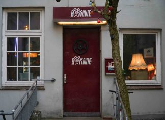 Kino günstiger als Netflix Eine Neonröhre wirft von oben Licht auf eine rote Tür, in deren Mitte eine Filmrolle hängt und die Aufschrift "B-Movie" zu lesen ist.