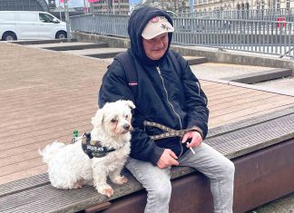 Früher obdachlos, heute Stadtführer Chris sitzt mit seinem Hund Struppi auf einer Bank. Zwischen seinen Fingern hält er eine Zigarette.