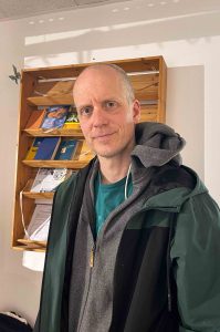 Der Teilnehmer Christoph Ernst steht im Hinz & Kunzt-Haus, hinter ihm hängt an der Wand ein Bücherregal.