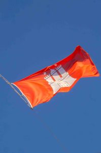 Eine rote Flagge mit dem Wappen der Hansestadt Hamburg flattert im Wind.