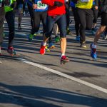 Halbmarathon wegen Hitze abgesagt Mehrere Menschen laufen bei einem Marathon über eine Asphalt-Straße. Das Bild ist oben abgeschnitten, sodass man nur die untere Häkfte der Menschen sieht. Sie tragen Sportkleidung und haben teilweise Schilder mit Zahlen auf ihren T-Shirts.