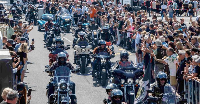 Viele Motorradfahrer*innen fahren in Reihen über eine Straße in der Sonne.