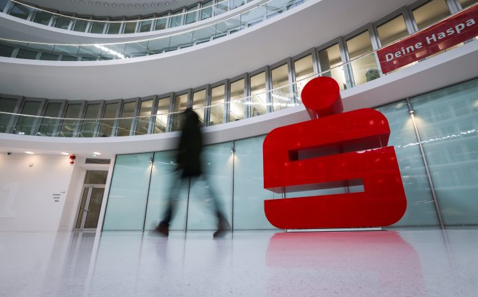 Eine Eingangshalle der Hamburger Sparkasse mit dem Logo der Sparkasse. Im Vordergrund sieht man eine Person, die durch die Halle läuft.