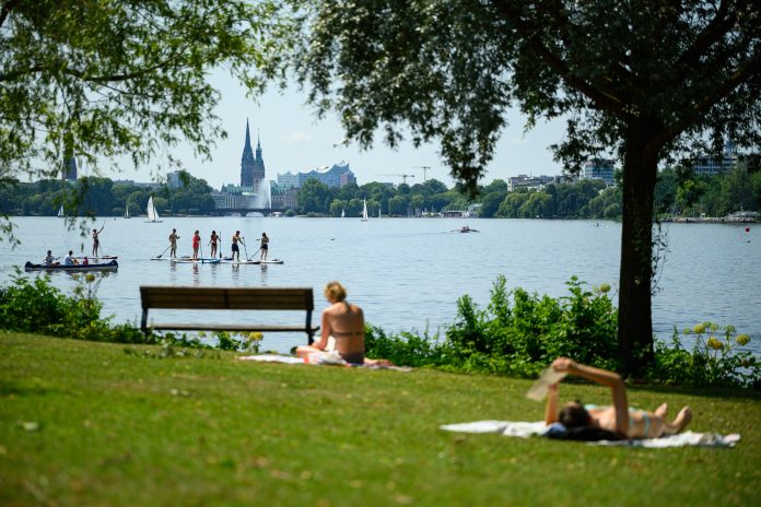 Hamburg: Menschen genießen auf und an der Außenalster vor der Stadtkulisse mit Alsterfontäne, Rathaus, Mahnmal St. Nikolai und Elbphilharmonie das Wetter.