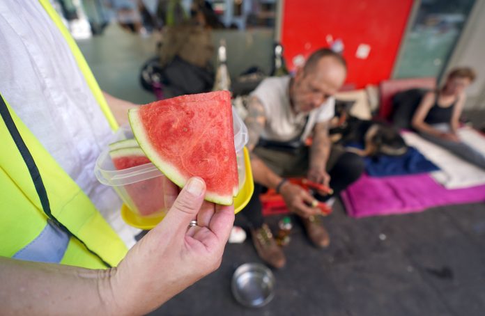 Obdachlose Menschen in Hamburg werden bei Hitze unterstützt. Helfer hält Wassermelone in der Hand.