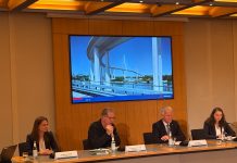 So soll die neue Köhlbrandbrücke aussehen 4 Personen sitzen in einer Pressekonferenz. auf einem Bildschirm hinter ihnen ist eine Visualisierung des Entwurfs der neuen Köhlbrandbrücke zu sehen.
