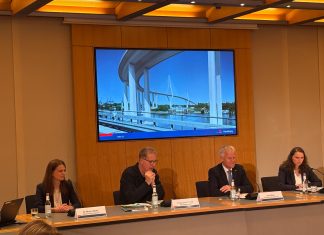 So soll die neue Köhlbrandbrücke aussehen 4 Personen sitzen in einer Pressekonferenz. auf einem Bildschirm hinter ihnen ist eine Visualisierung des Entwurfs der neuen Köhlbrandbrücke zu sehen.