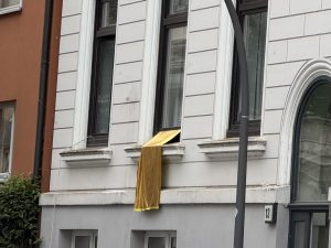 Eine goldene Stoffbahn hängt aus einem Fenster eines Ottenser Wohnhauses.