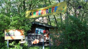 Der Kindertreff im HausDrei. Es ist ein Spielplatz draußen, über dem ein gelbes Schild mit "Kindertreff" hängt.