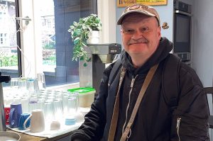 Chris steht in der Küche im Hinz & Kunzt-Haus. Hinter ihm stehen viele Tassen. Er lächelt.