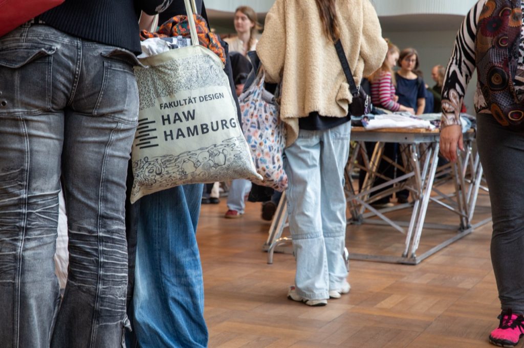 Viele Menschen besuchen die Kleidertauschparty der HAW Hamburg. Sie stehen um die Tische mit Kleidung herum.