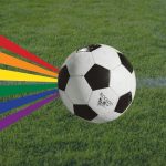 Queeres Public Viewing der WM im Gängeviertel Ein Fußball ist auf Rasen zu sehen mit einer Regenbogenflagge. Die Regenbogenflagge steht unter anderen für queere Personen. Das Public-Viewing ist für sie ausgelegt.