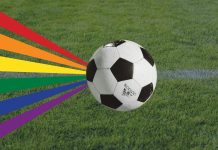 Queeres Public Viewing der WM im Gängeviertel Ein Fußball ist auf Rasen zu sehen mit einer Regenbogenflagge. Die Regenbogenflagge steht unter anderen für queere Personen. Das Public-Viewing ist für sie ausgelegt.