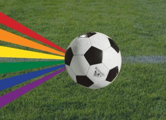 Queeres Public Viewing der WM im Gängeviertel Ein Fußball ist auf Rasen zu sehen mit einer Regenbogenflagge. Die Regenbogenflagge steht unter anderen für queere Personen. Das Public-Viewing ist für sie ausgelegt.