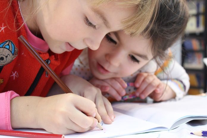 Zwei Kinder schauen auf ein Schulheft und schreiben darin.