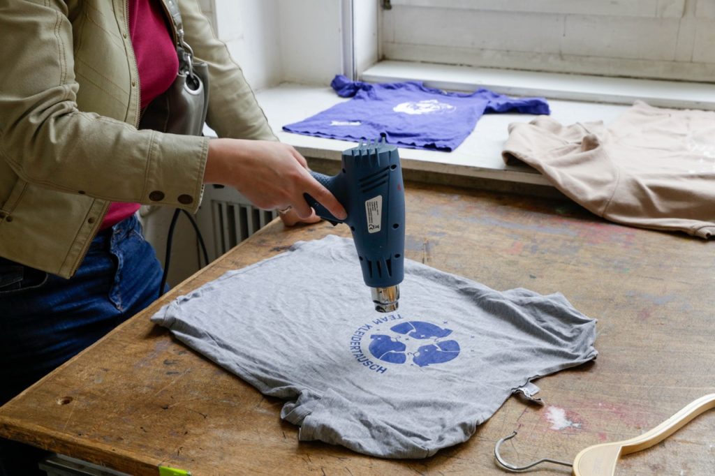 An der Siebdruck-Station wird ein Motiv auf einem T-Shirt mit einem Föhn fixiert.
