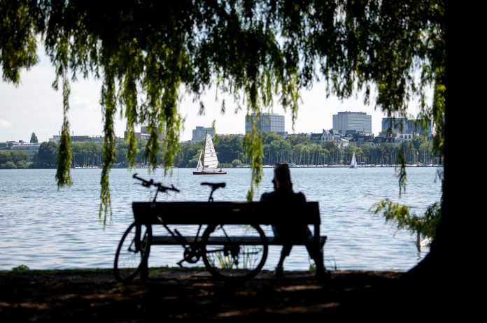 Sommerliches Wetter in Hamburg Hamburg: Ein Mann sitzt im Schatten eines Baumes an der Außenalster auf einer Bank.