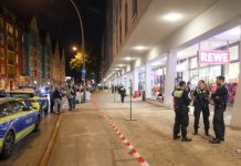 Messerattacke in Altonaer Supermarkt endet tödlich EIn Polizeiauto steht an einem Bürgersteig wo eine Gruppe an Polizist*innen vor einem Rewe stehen im Kontext einer Messerattacke