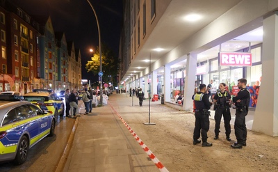 Streit in Supermarkt in Hamburg führt zu Messerattacke EIn Polizeiauto steht an einem Bürgersteig wo eine Gruppe an Polizist*innen vor einem Rewe stehen im Kontext einer Messerattacke