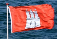 Wo bleibt der Sommer? Rote Hamburg-Flagge weht im Wind. Im Hintergrund ist welliges Wasser zu sehen.