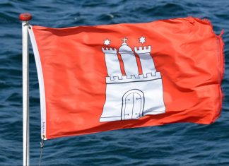 Wo bleibt der Sommer? Rote Hamburg-Flagge weht im Wind. Im Hintergrund ist welliges Wasser zu sehen.