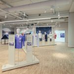 „Warum ist sie nicht gegangen?“ Sport im Nationalsozialismus Der Ausstellungsraum mit Informationstafeln an den Wänden und Figuren mit Trikots in der Mitte des Raumes.