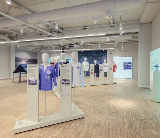 „Warum ist sie nicht gegangen?“ Sport im Nationalsozialismus Der Ausstellungsraum mit Informationstafeln an den Wänden und Figuren mit Trikots in der Mitte des Raumes.