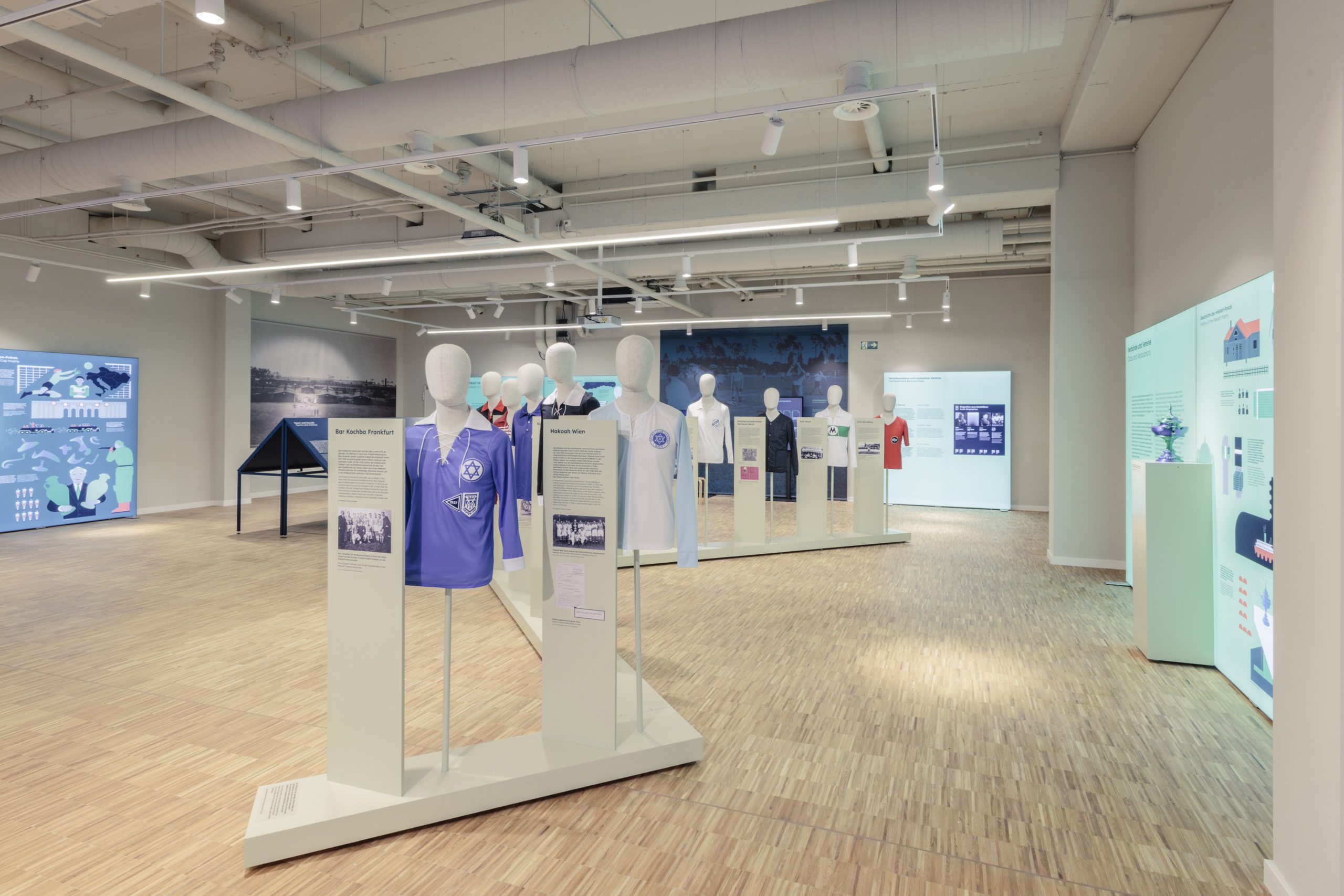 blick-in-die-ausstellung-sport-masse--macht-im-kultur-kontor-hamburg-foto-jerome-gerull-shmh-1 Der Ausstellungsraum mit Informationstafeln an den Wänden und Figuren mit Trikots in der Mitte des Raumes.
