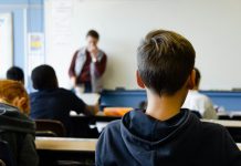 Ethik statt Religion – auch schon für Grundschulen Ein Kind im Vordergrund, welches man von hinten sieht und im Hintergrund ein Lehrer vor einer Tafel. Die GEW möchte, dass Alternativen zum Religionsunterricht ab der ersten Klasse schon angeboten werden.
